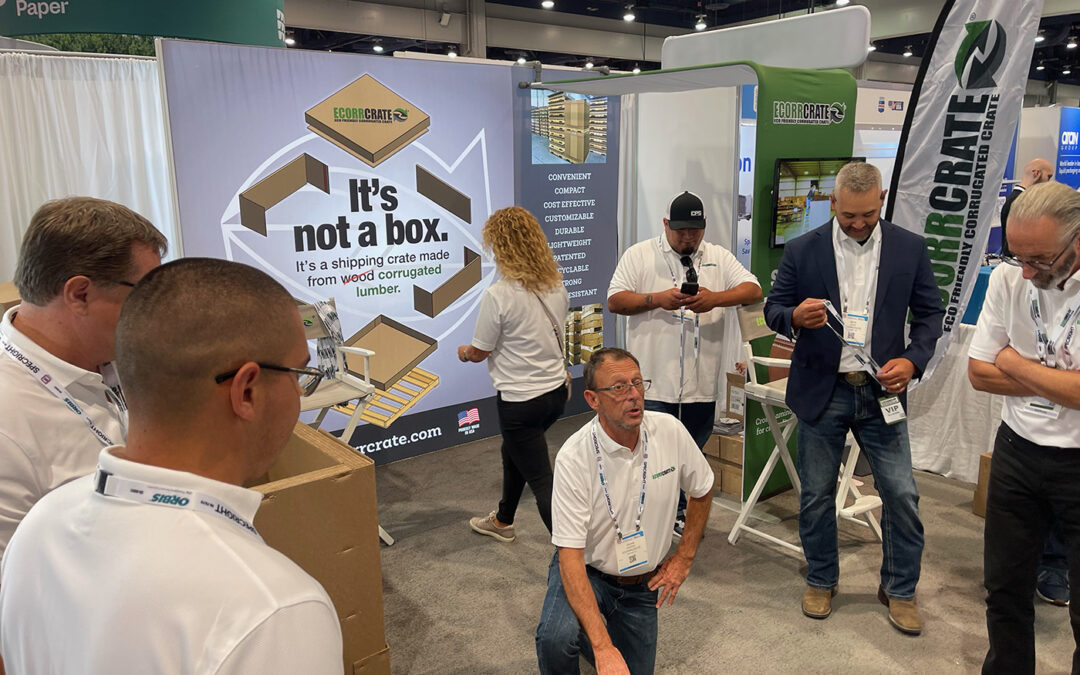 man kneeling on ground to show knocked down version of an Ecorrcrate to trade show attendees at Pack Expo with a banner in the background saying "it's not a box"