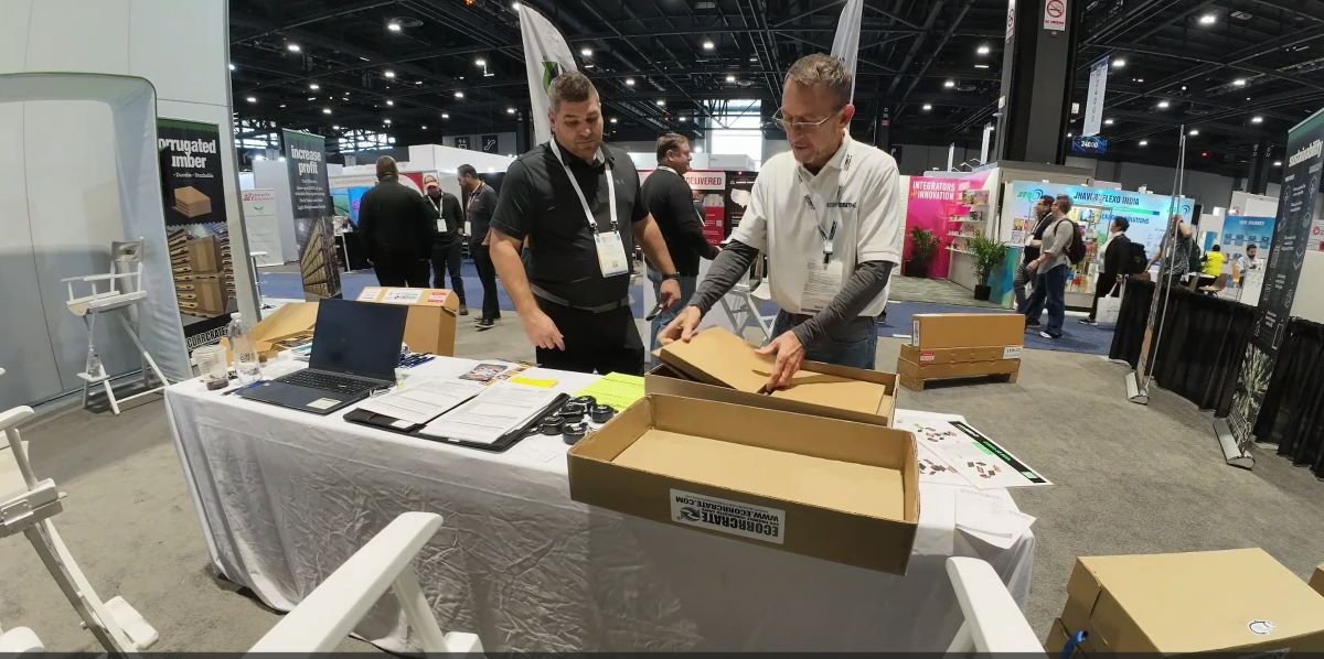 Showing a potential client how an ecorrcrate sample and various components. Multiple customers in background perusing booth. Ecorrcrate's booth at the MRO Americas Pack Expo show 2024